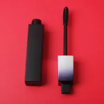 Cosmetic mascara standing upright beside its applicator